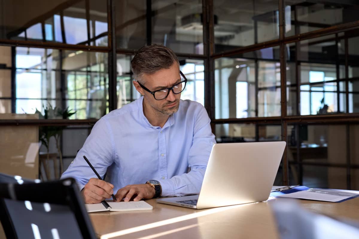 Hombre adulto de negocios mirando un computador y escribiendo en un cuaderno en una oficina