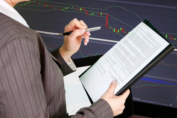 Broker con una hoja con información en su mano y analizando índices financieros.