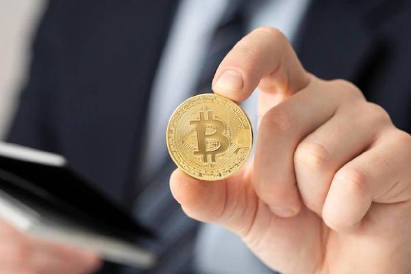Un trader sostiene en su mano una Bitcoin.
