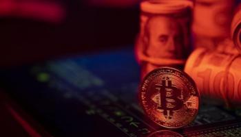 Una BTC junto a billetes de 100 dólares. Descubre lo que debes saber antes de comprar Bitcoin.