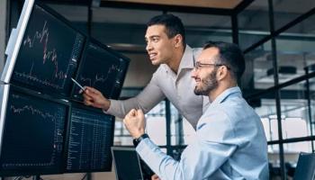 Dos traders hombres felices viendo en las pantalla de su oficina los beneficios del trading y resultados