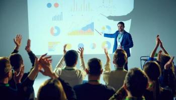 Conferencia de trading exitosa con público y expositor felices frente a una pantalla