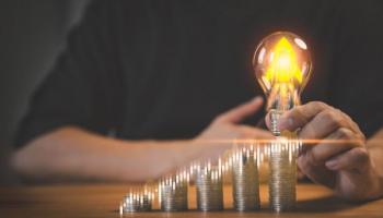 Persona con un foco sobre grupos de monedas en aumento representando el crecimiento de una inversión
