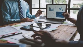 Personas en una oficina discutiendo y analizando los tipos de mercados financieros y datos de mercado en una computadora portátil